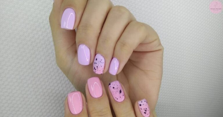 a hand showcasing stylish hot pink nails with abstract black ink splatter designs on three nails and delicate white line accents