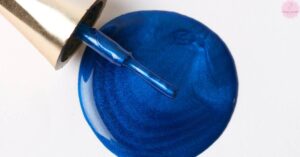 a close-up of a royal blue ombre nail with a glossy top coat, being detailed with a precision nail art sponge tool.