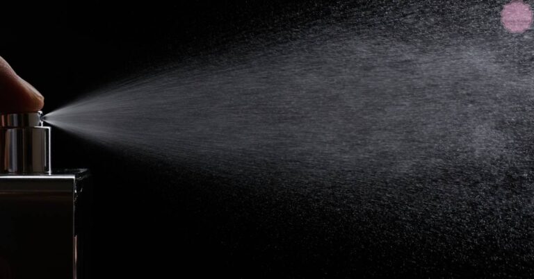 a close-up of a perfume atomizer spraying mist against a dark textured background