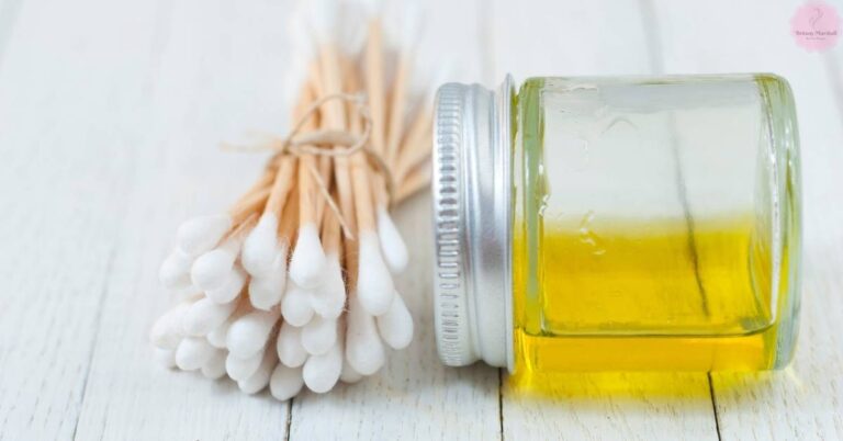 a bundle of cotton swabs tied with twine next to a jar filled with clear yellow baby oil for tanning