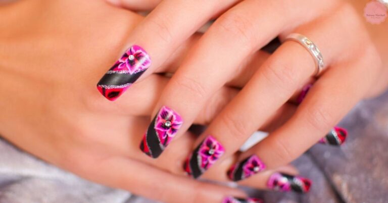 a hand showcasing stylish overlay nails with black base, pink floral designs, and glitter accents on elongated nails