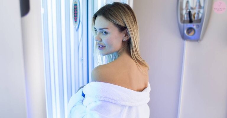 a woman in a robe standing inside a tanning booth with a relaxed expression, showcasing a healthy glow from controlled sun exposure.