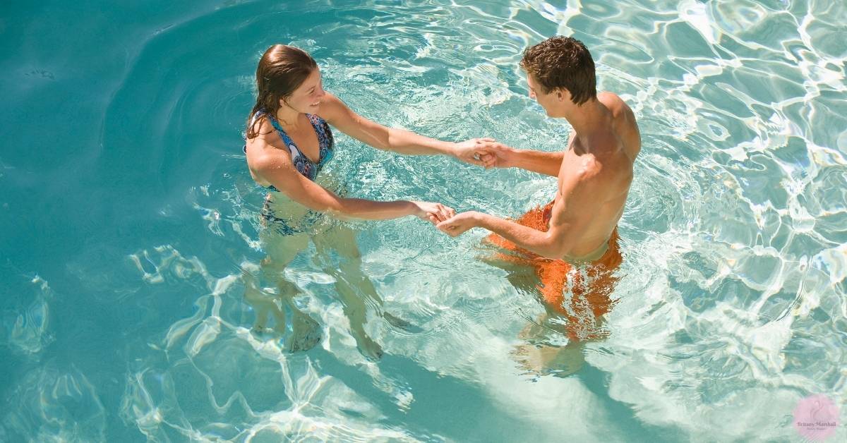 a couple holding hands while enjoying a refreshing swim in clear pool water, basking in a sunlit environment