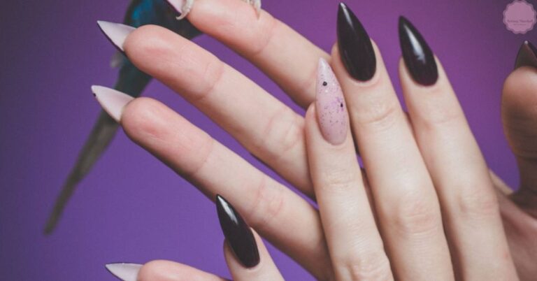 a hand holding a nail file with long acrylic nails, one featuring a speckled design and others painted black
