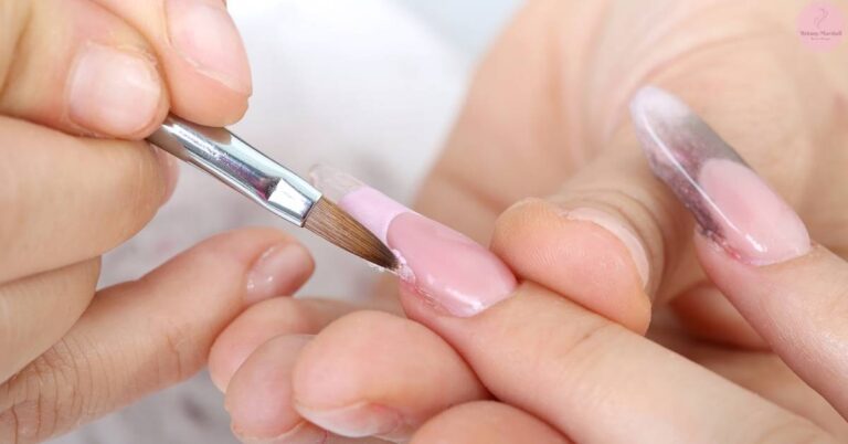a person carefully using an acetone-soaked cotton swab to remove dip powder nail polish from a fingernail at home