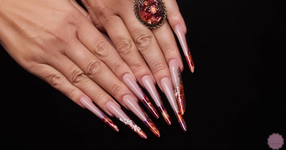 a pair of hands showcasing long, elegantly styled acrylic nails with glittery red and gold accents on tips