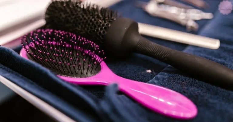 a pink hairbrush with glittery bristles and a matching comb, placed on a dark textured surface alongside hair care tools for cleaning and maintenance