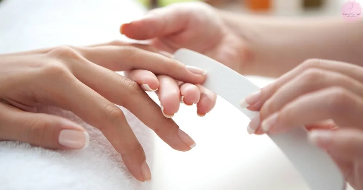 a pair of hands gently holding another person’s hand during a professional nail care treatment, showcasing smooth, well-maintained nails.