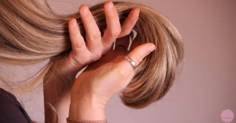 a person holding back long blonde hair to reveal potential dust or lint accumulation, examining hair strands closely.