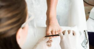 a medical professional examining a patient’s foot with a pen to assess abnormal toenail growth under a healthy toenail.