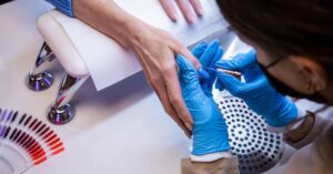 a nail technician in blue gloves applying gel polish to a client’s nails during a professional manicure service