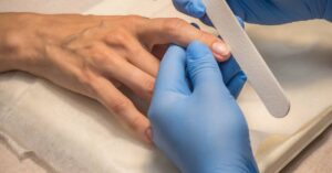 a gloved hand demonstrating nail curvature by pressing on a person’s flat nail plate to show natural nail bed flexibility