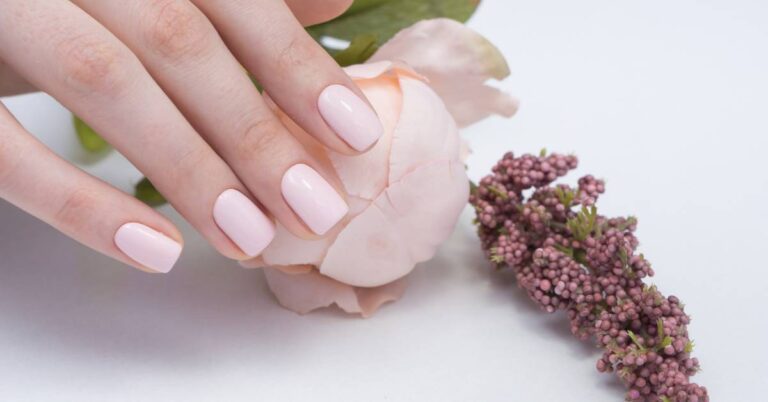 a hand gently holding a delicate white peony flower bud, showcasing neatly manicured nails with light pink polish, beside a sprig of lilac blossoms