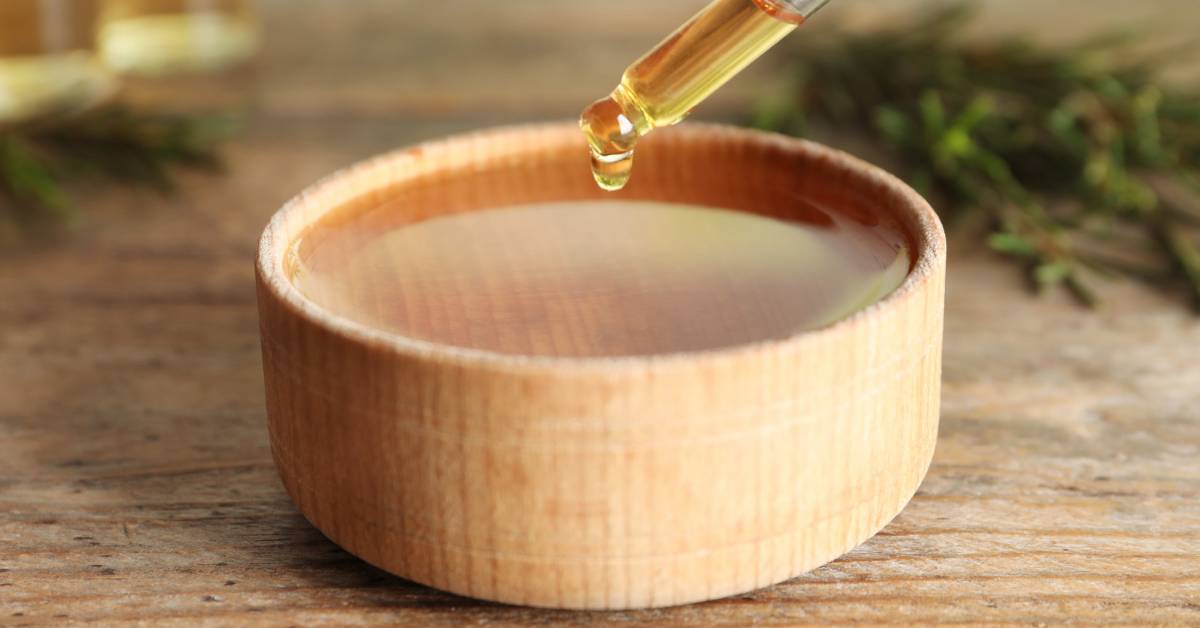 a wooden bowl with a dropper releasing diluted natural tea tree oil onto it, emphasizing proper dilution technique.