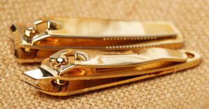 gold-toned straight-edge nail clippers with a pivoting blade for precise cutting, showcasing a sleek, compact design for nail care.