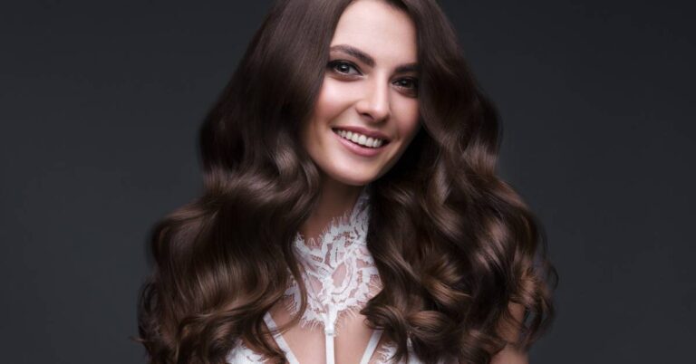 a woman with long, voluminous wavy hair and a radiant smile wearing a lace top, showcasing healthy, well-groomed lashes