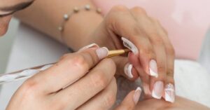 a professional applying a slip solution to freshly shaped polygel nails during a manicure process