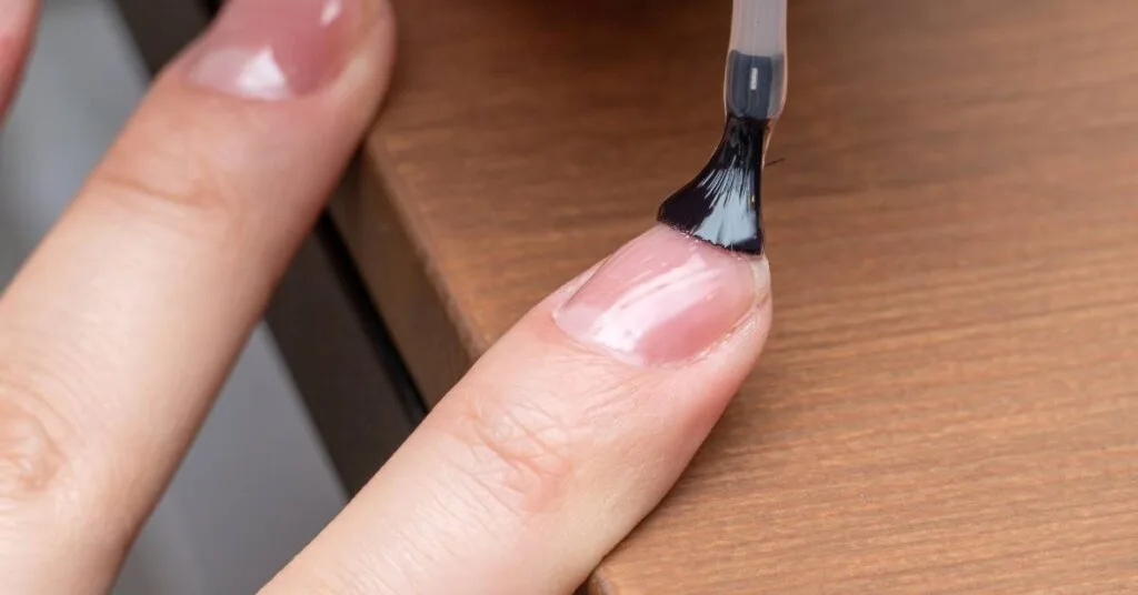 a hand applying nail primer to a fingertip for nail preparation before polish