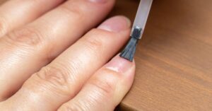 a hand using a nail primer brush to apply product to a fingernail for nail preparation