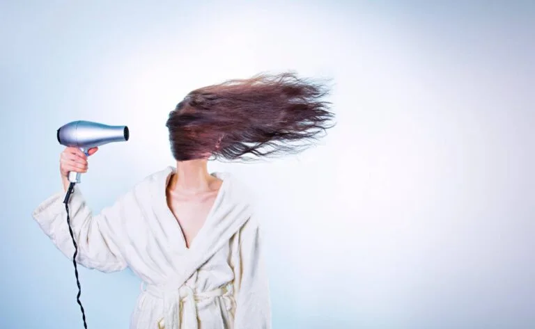 a person drying their long hair with a hair dryer while holding the cord, demonstrating potential extension cord risks.