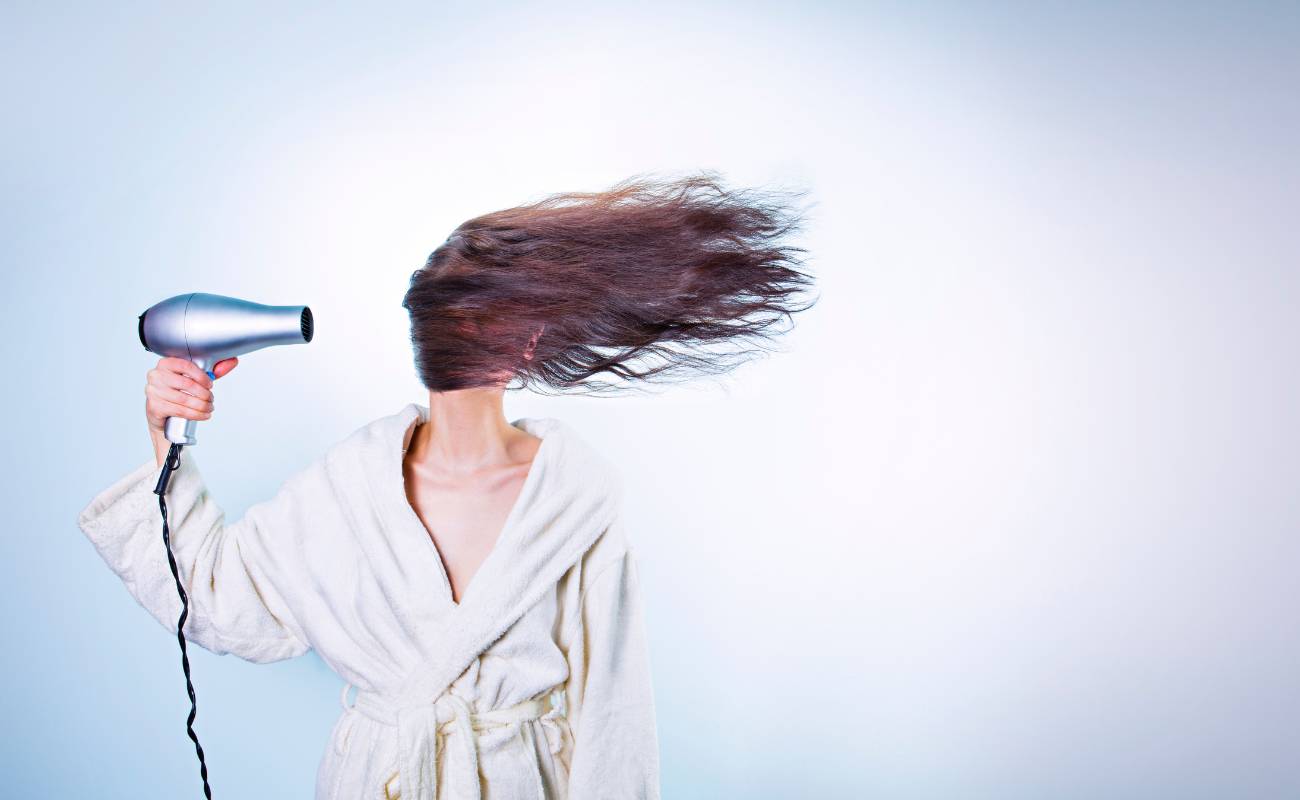 a person drying their long hair with a hair dryer while holding the cord, demonstrating potential extension cord risks.