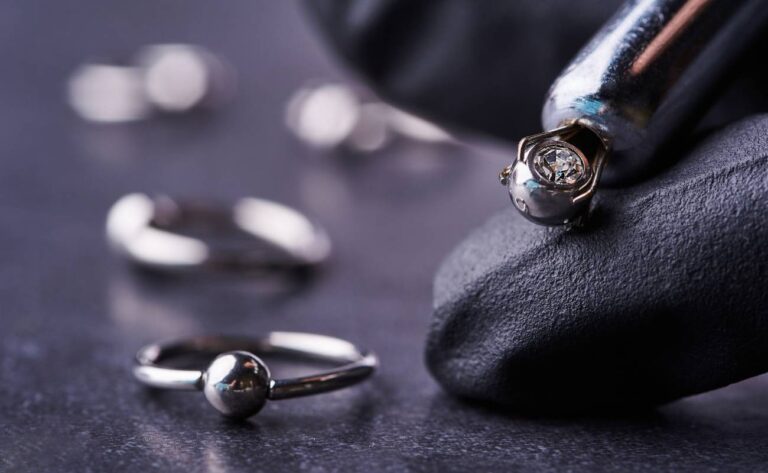 a close-up of a silver tooth piercing stud and ring jewelry on a dark textured surface, highlighting potential entry points for oral health concerns.