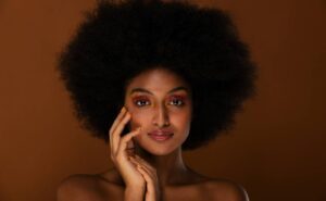 a woman showcasing bold editorial makeup with voluminous afro hair, poised elegantly for a high-fashion photo shoot.