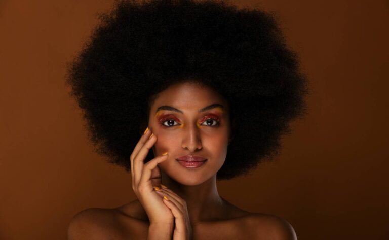 a woman showcasing bold editorial makeup with voluminous afro hair, poised elegantly for a high-fashion photo shoot.